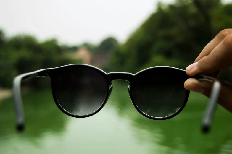 a person holding onto some sunglasses near the water