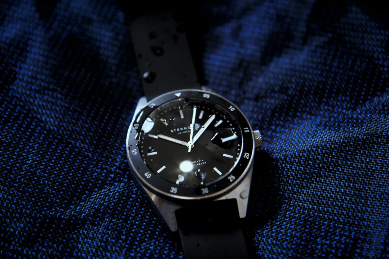 an elegant, stainless steel watch sits on a dark blue blanket