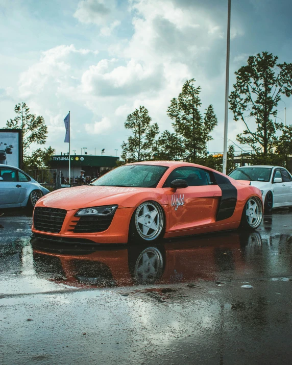 an orange car with its hood on sits on a wet street