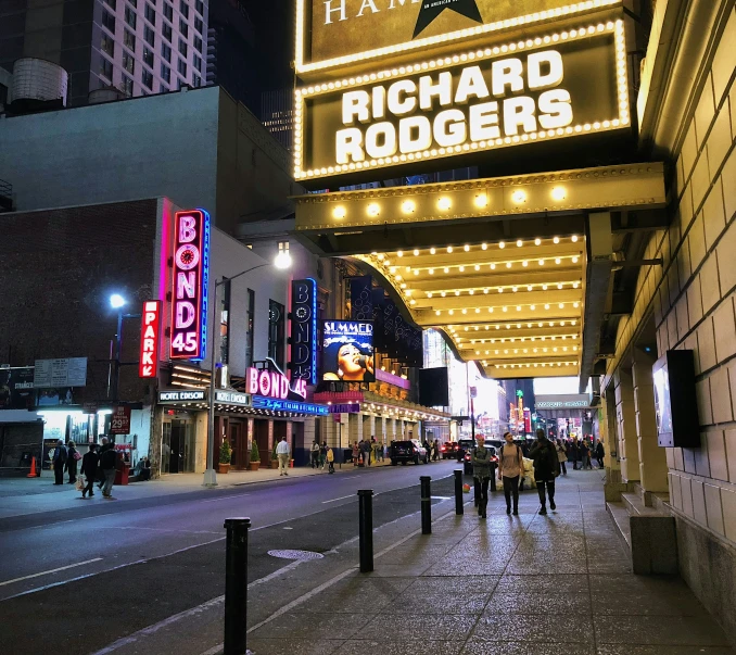 people walking on the street underneath a sign for a concert theater