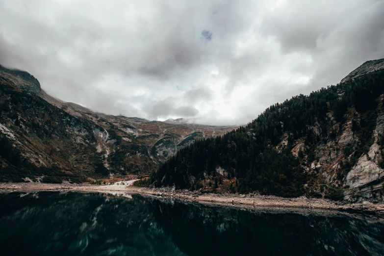 a landscape of some mountains, in the foreground, with water, and some clouds