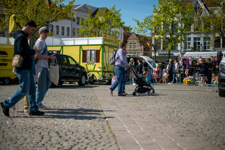 some people walking along a street in front of parked cars