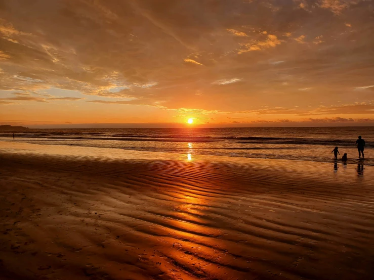 a person is walking on the beach during sunset