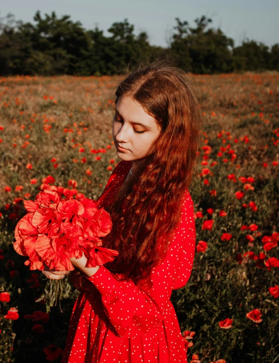 a woman wearing a red dress is standing in a field holding a bouquet of red flowers