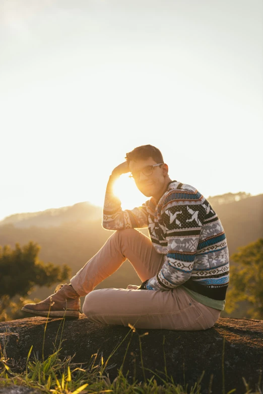 a young man with glasses is sitting on a rock looking into the distance