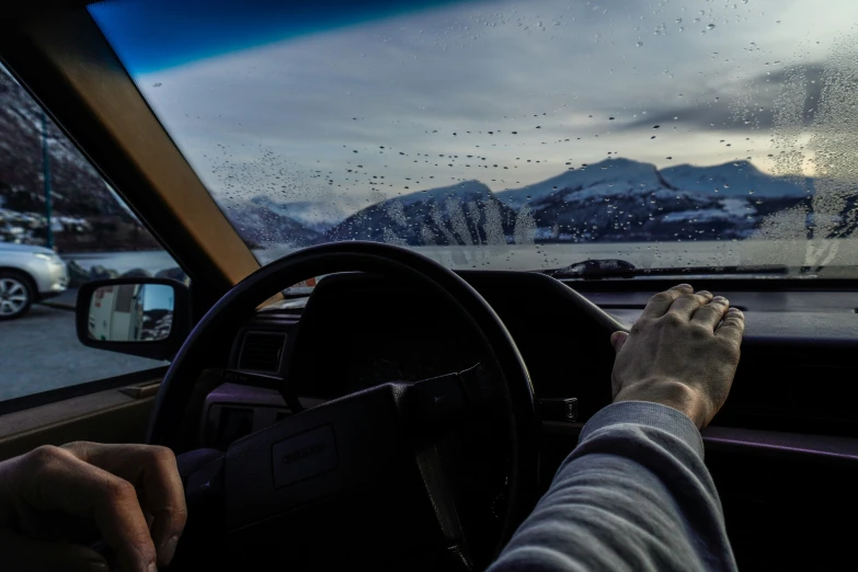 a person driving on a rainy road with mountains in the background