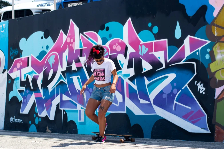 a woman standing on a skateboard next to a wall with graffiti