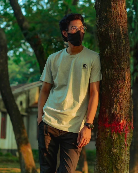 a young man with glasses leaning on a tree