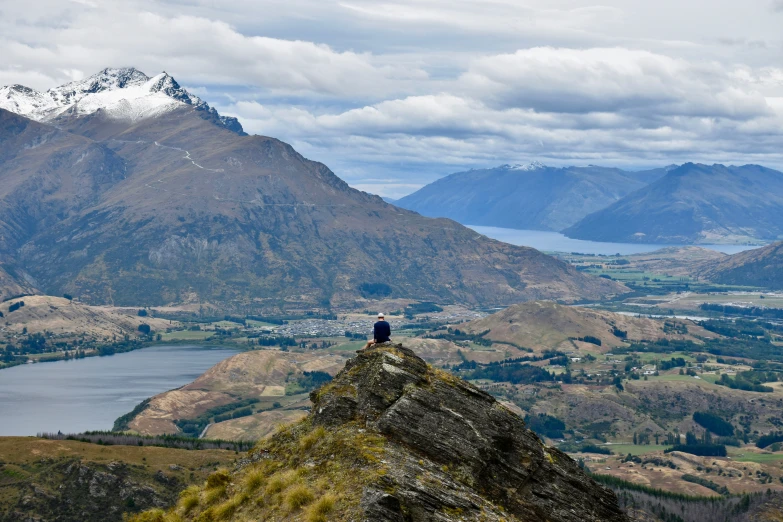 a lone person standing on a mountain ledge overlooking a large lake