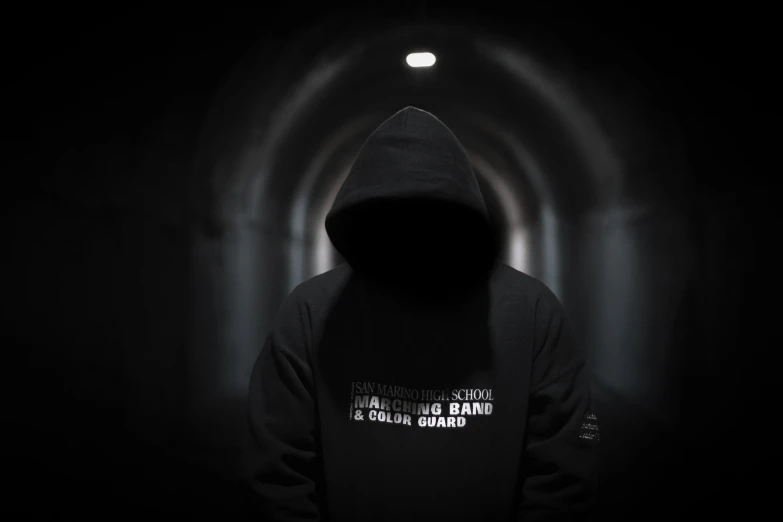 a dark hooded man in a tunnel wearing a hooded jacket