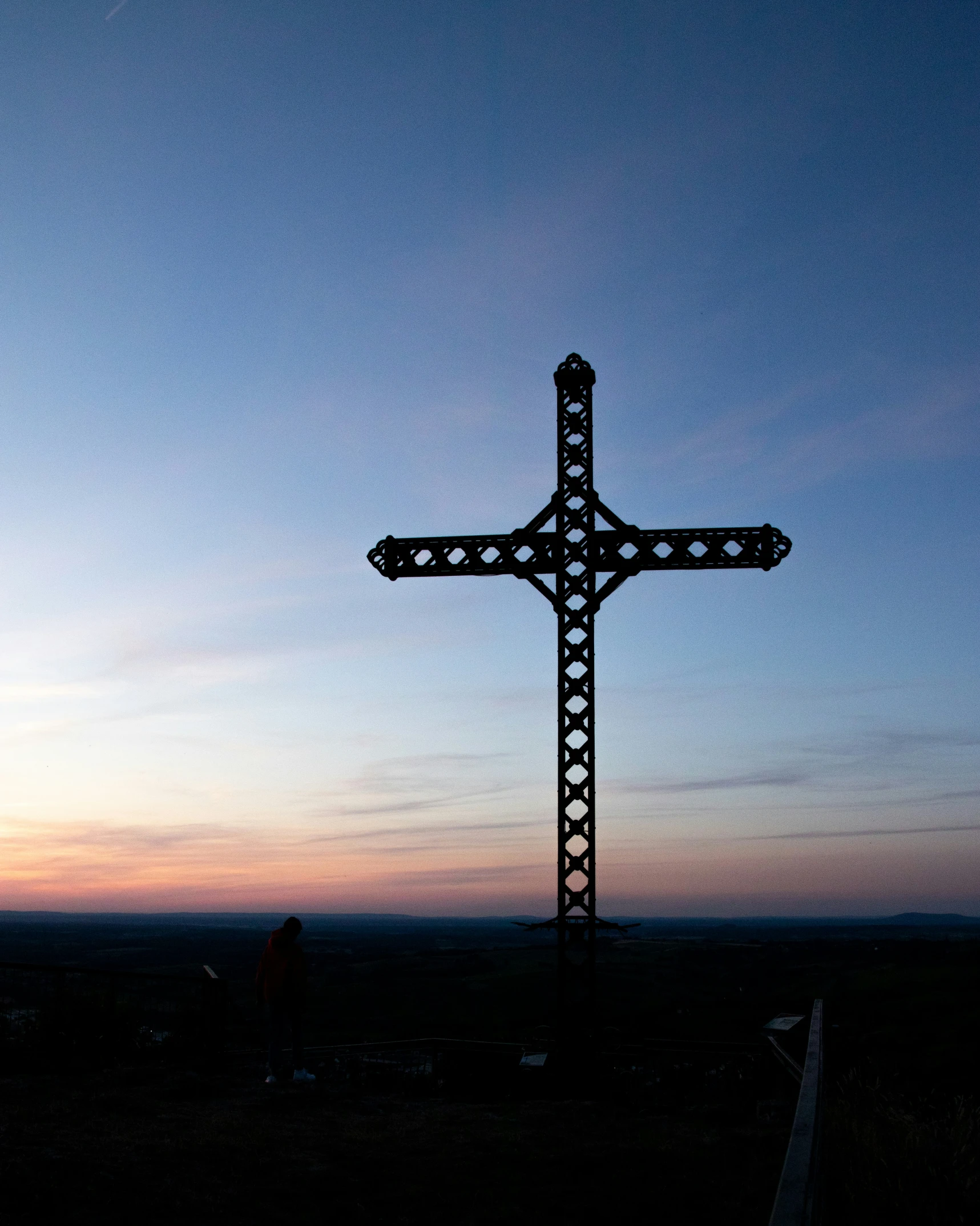 a tall metal cross on the side of a road