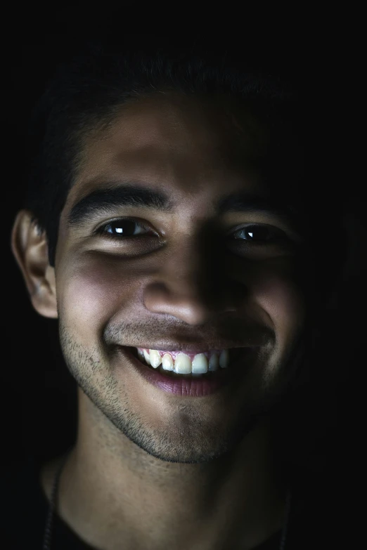 a man smiling for the camera with dark lighting
