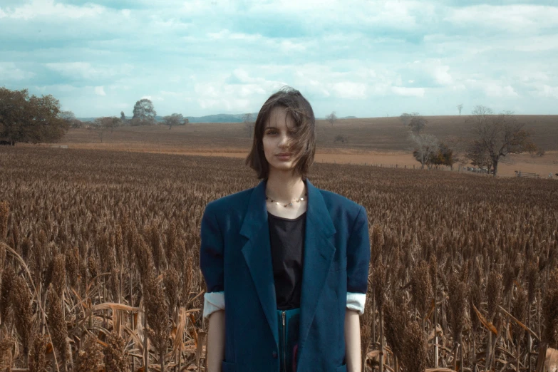 a girl stands in front of a cornfield