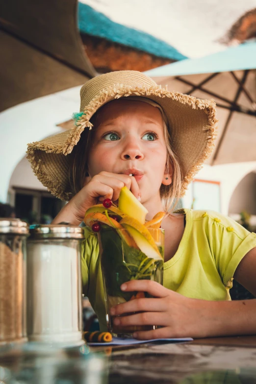 little girl in yellow top wearing straw hat biting into banana