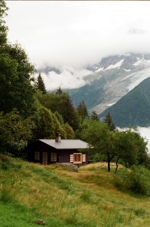 a cabin nestled on a hillside with the mountains in the background