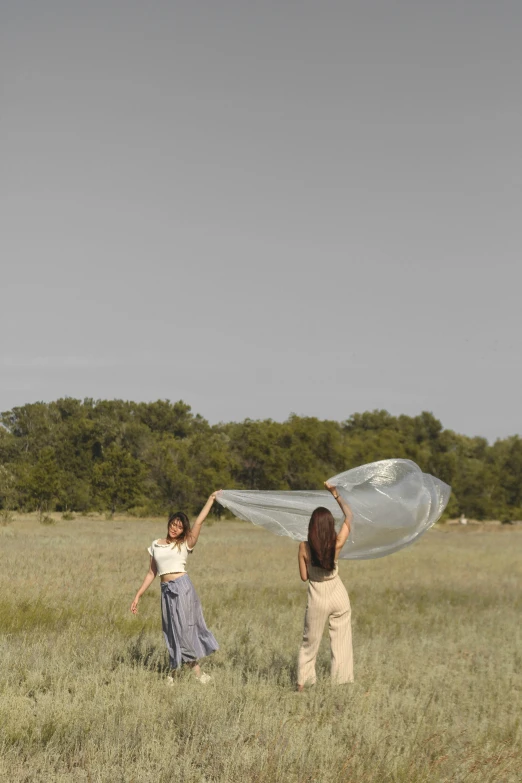 two women playing with a white kite in a field