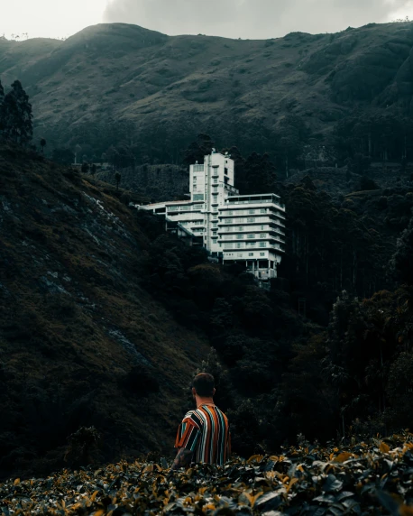 a man sitting in a hill looking at a large building