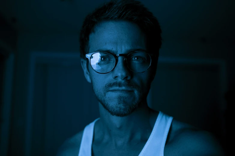 man with glasses wearing tank top in dark room