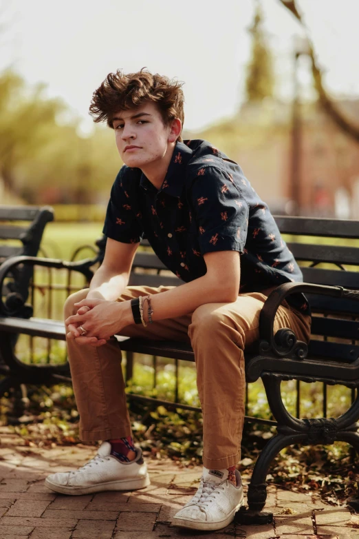 a young man sits on a park bench, holding his hand out