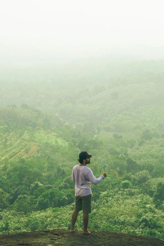 a man standing on top of a hill near lush green forest