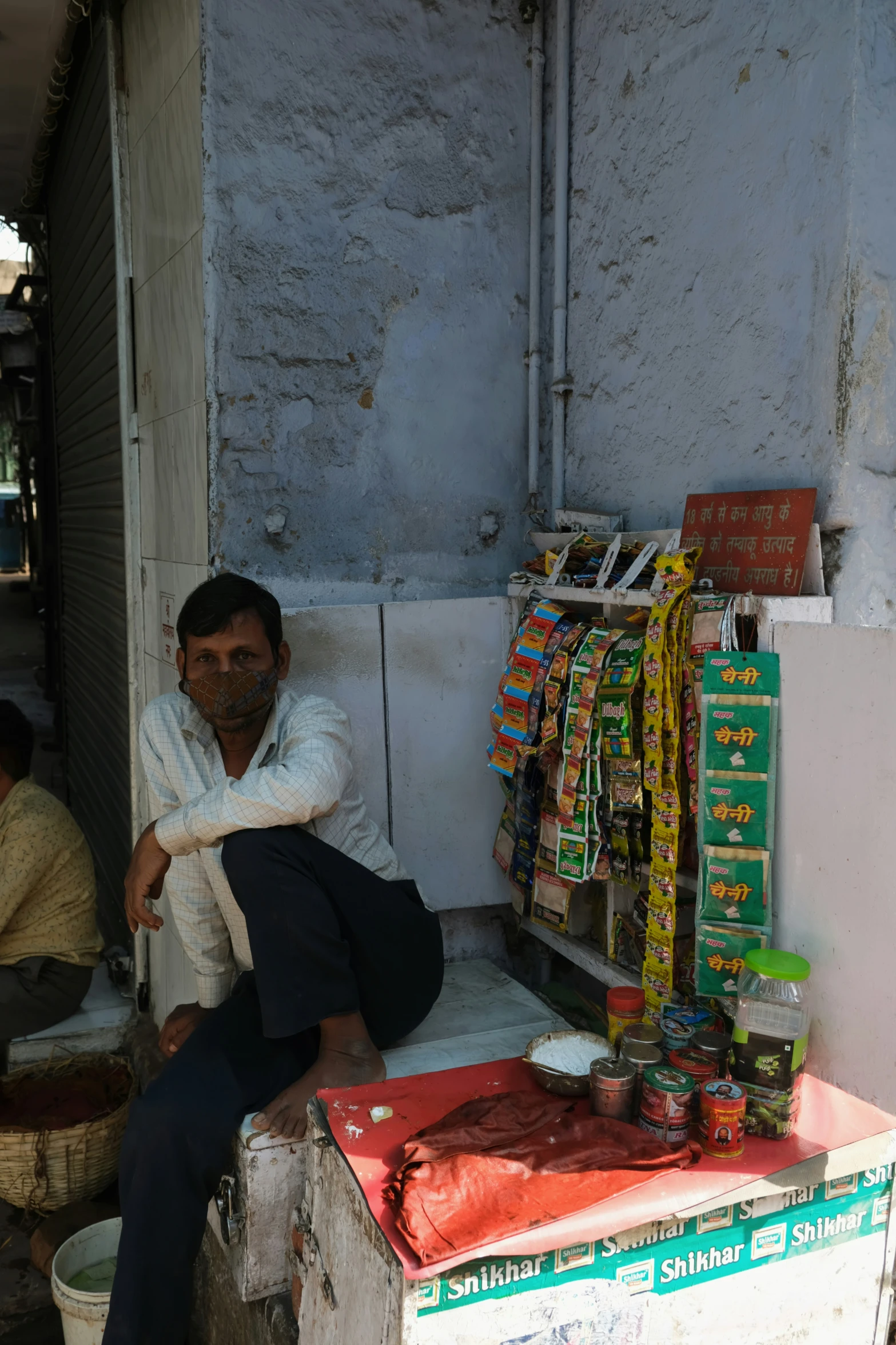 a man sitting on a small outdoor stand selling goods