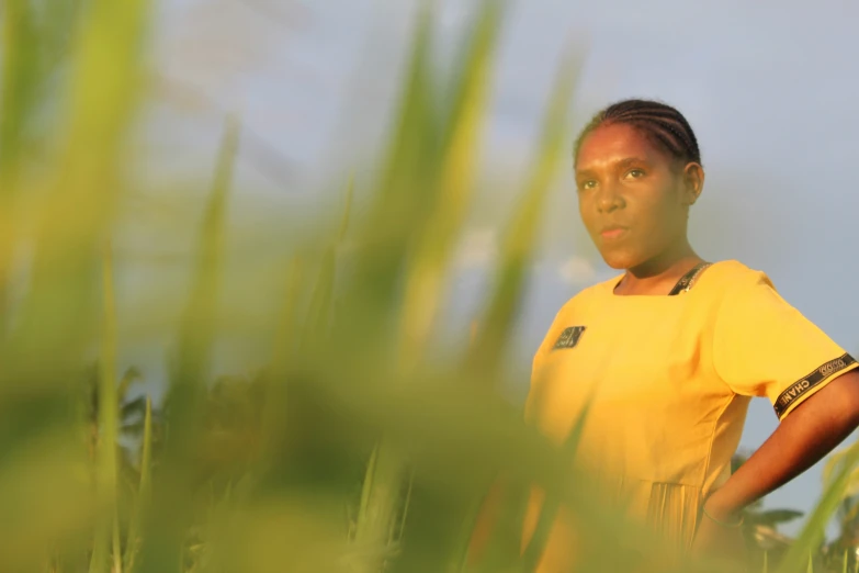 a girl in a yellow shirt is standing in tall grass