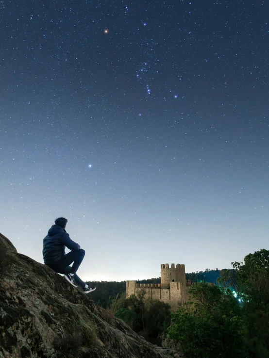 a man sitting on a hill under the night sky