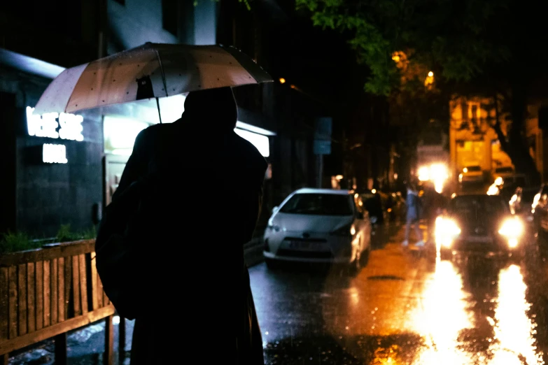 there is a person standing on the sidewalk at night under an umbrella