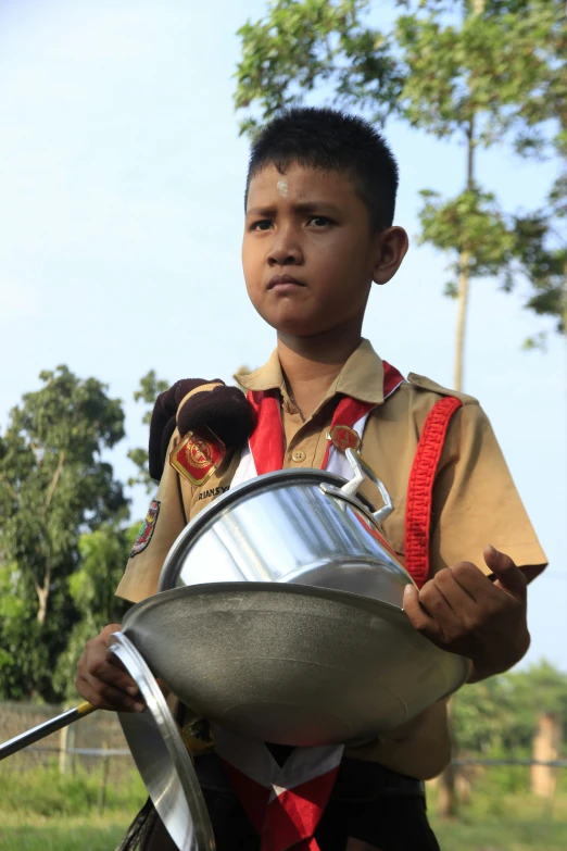 a boy dressed in uniform with a big metal pan