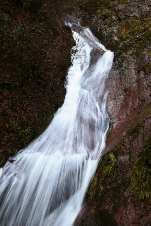 a waterfall flowing from one cliff near a grass covered hillside