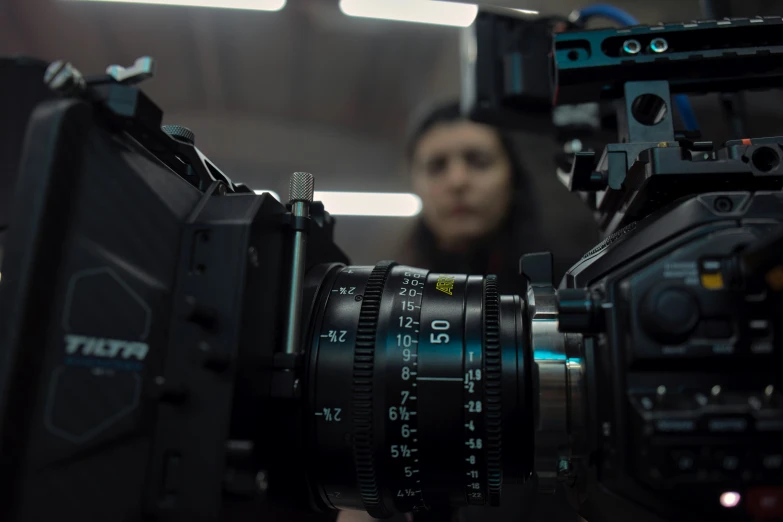 a camera sits on a tripod with a woman standing behind it