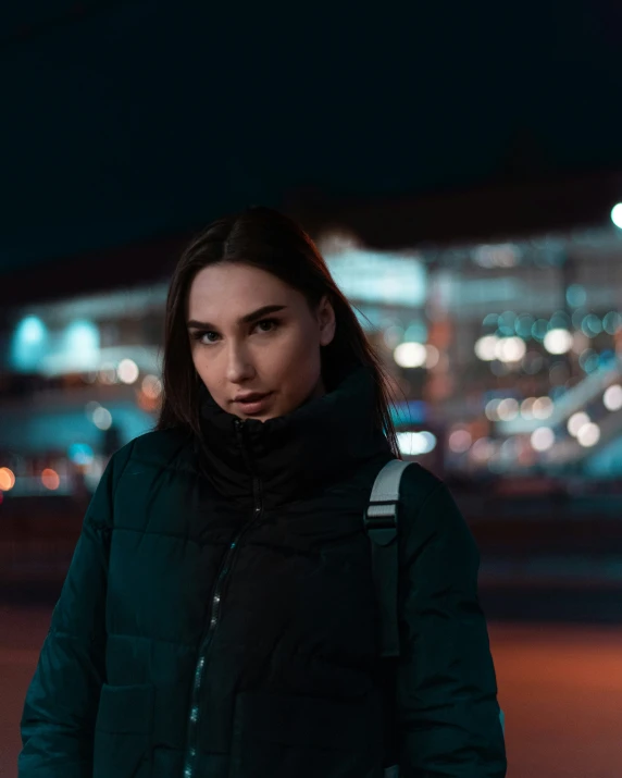 a young woman standing outside at night wearing a coat and a backpack