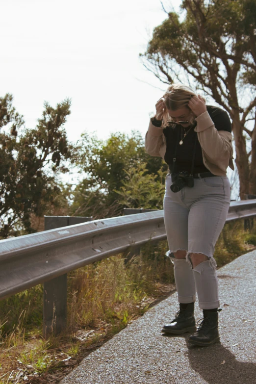 a woman in ripped jeans leans against a fence