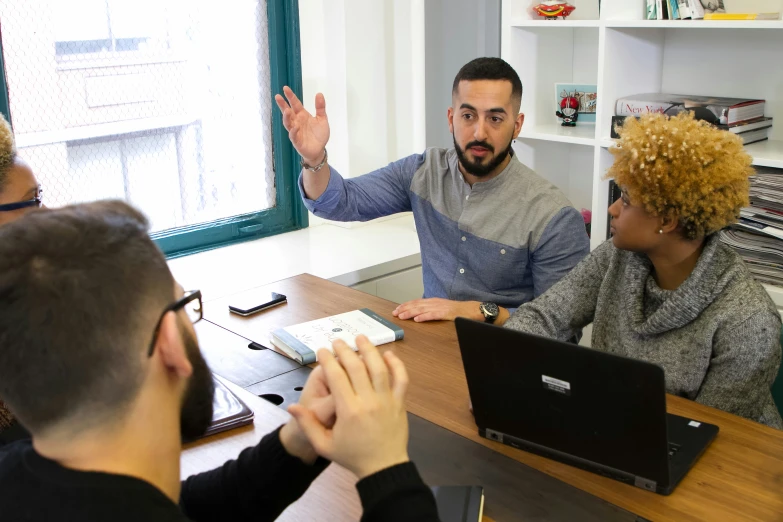 four people are sitting around a table with one is on a laptop