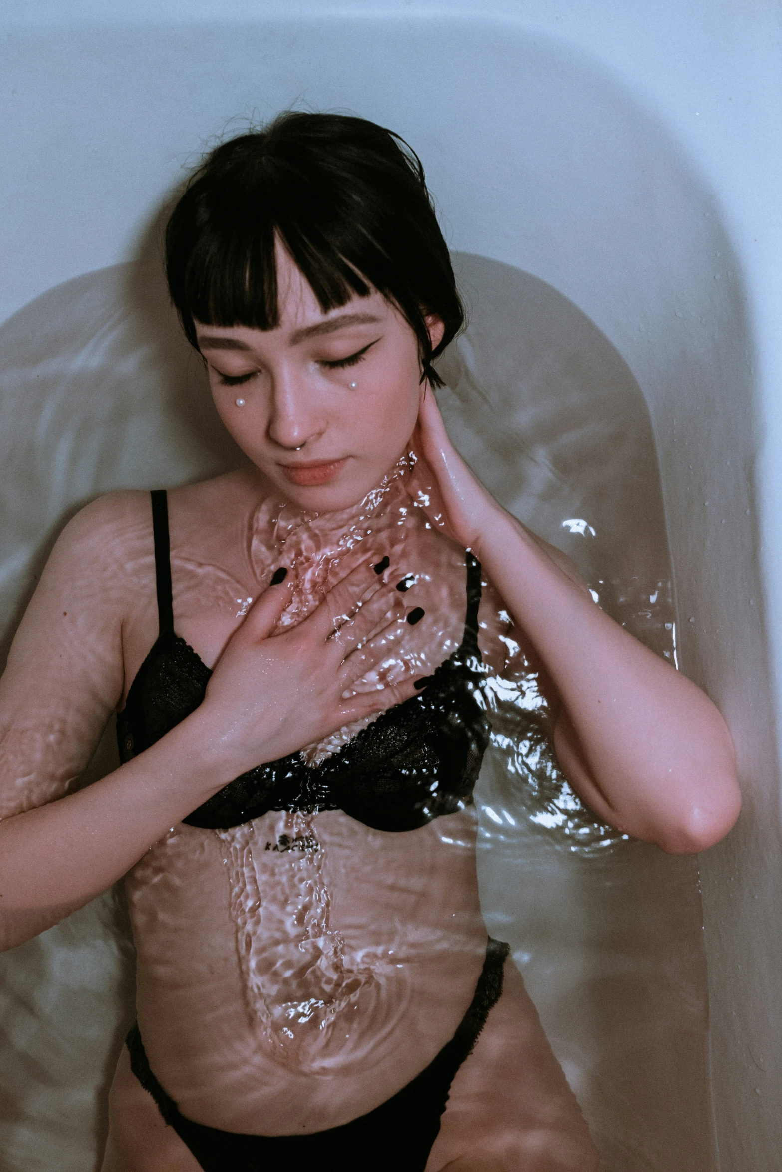 woman in black underwear sitting in tub with lots of bubbles all over her face