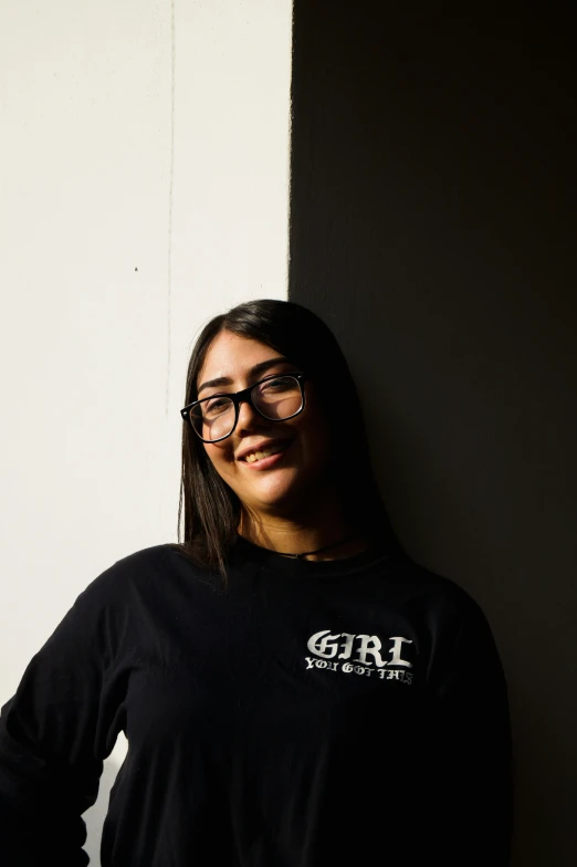 a young woman wearing a long sleeve black shirt smiling and leaning against a wall