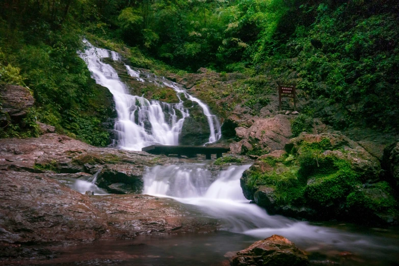 a waterfall next to a cliff filled with green trees