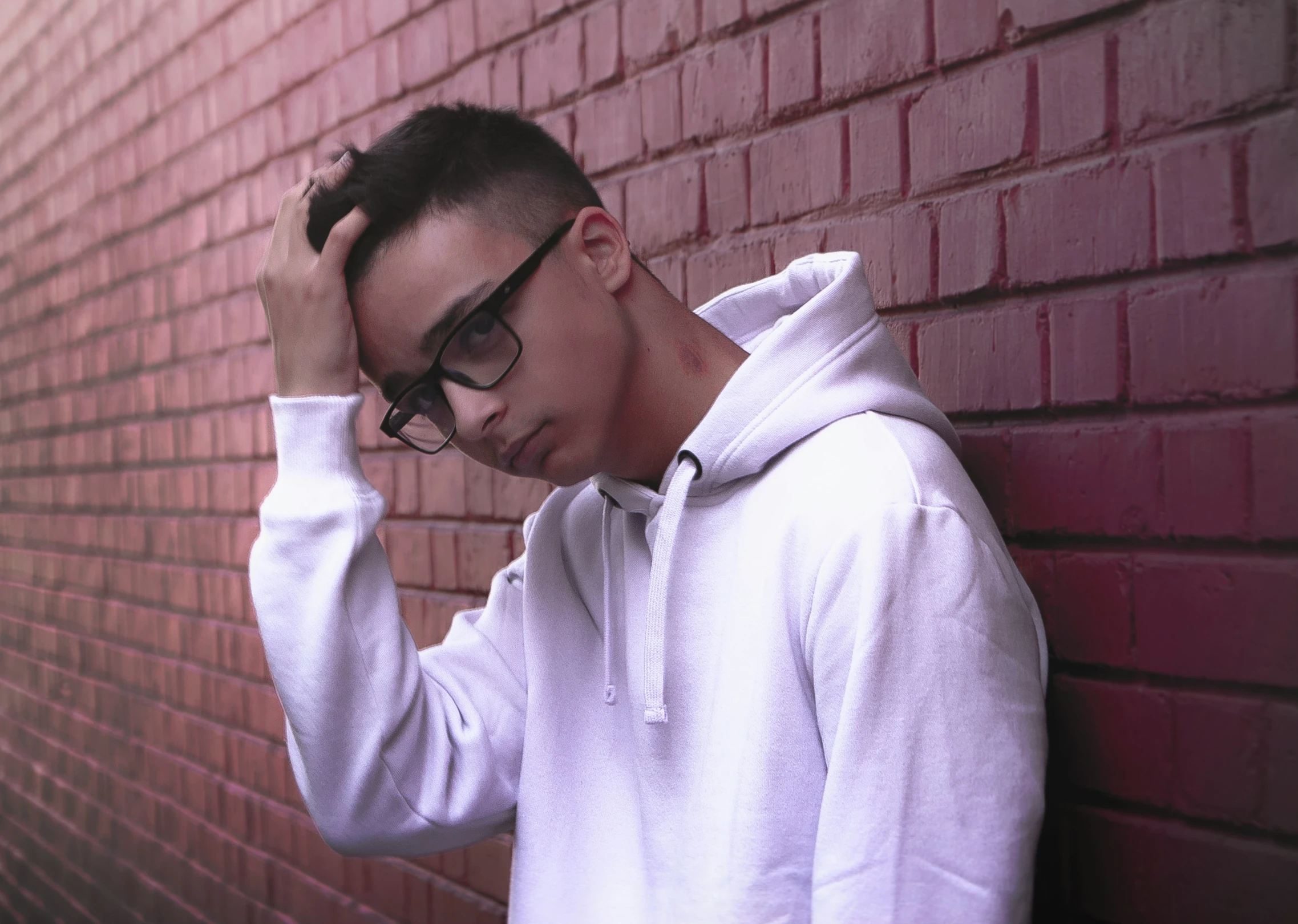 a man in glasses leaning against a brick wall