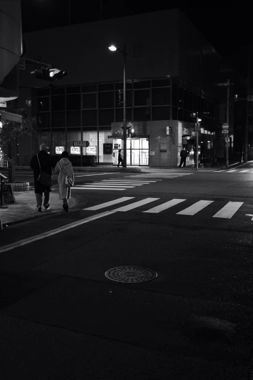 two people crossing a street at night with an umbrella