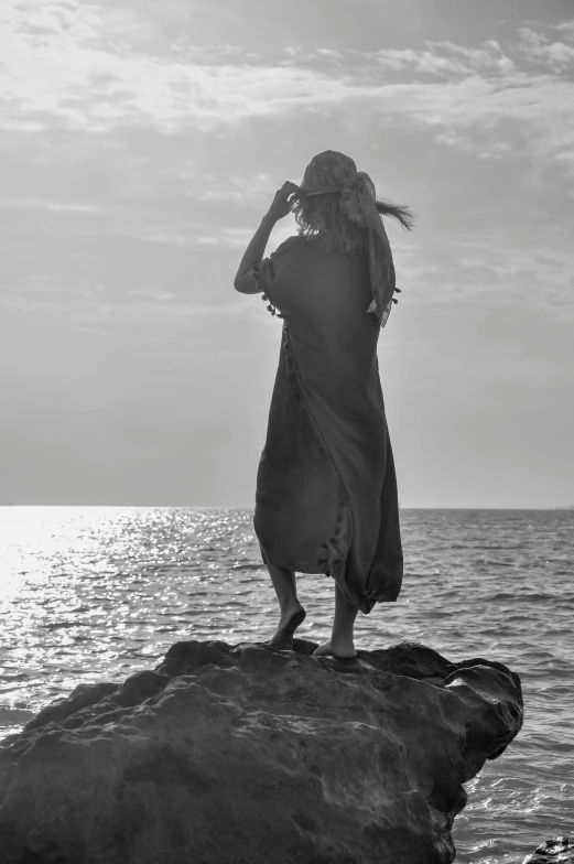 a woman standing on top of a rock near the ocean