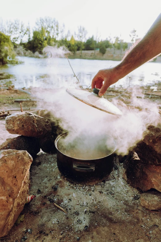 a man is using a wok to cook food on a campfire