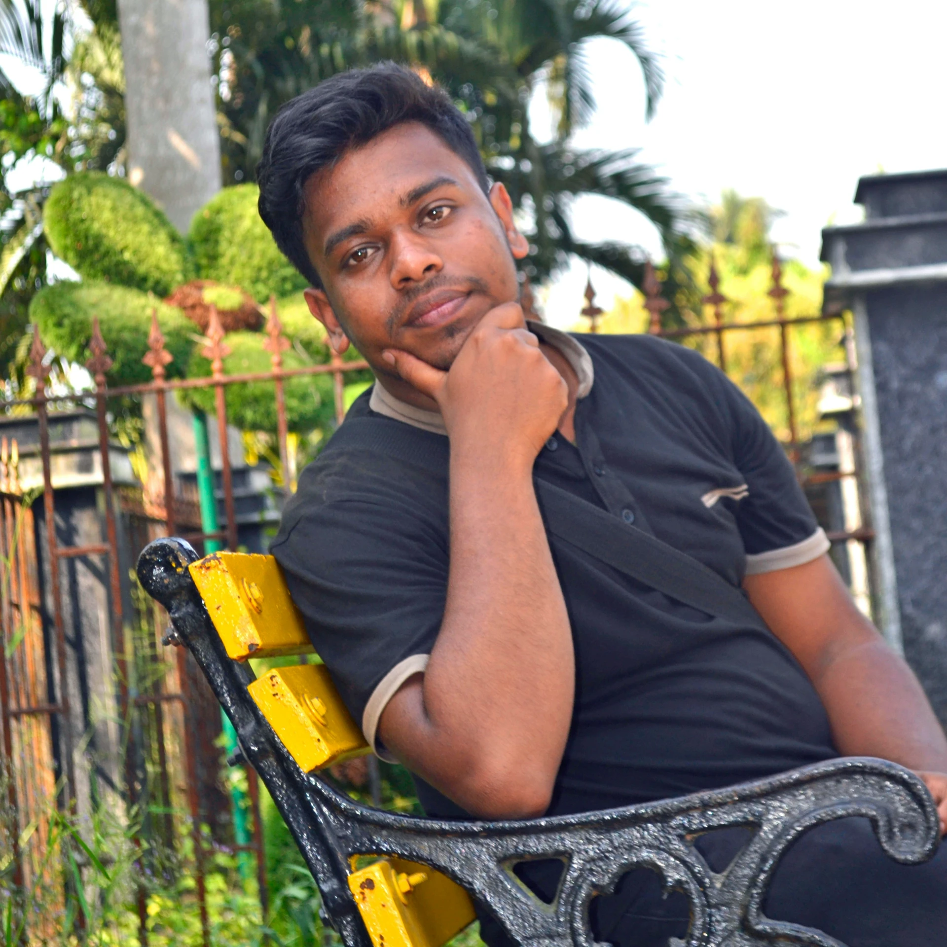 a man is sitting in a park holding his chin on a yellow bench