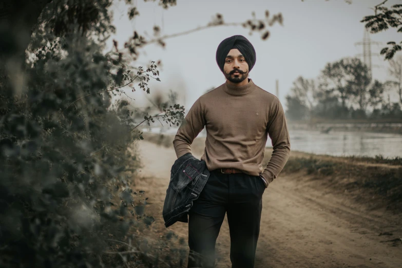 the man is standing in a wooded area wearing a brown sweater