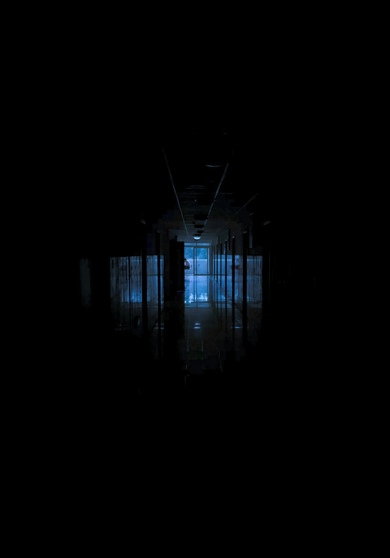 a dark hallway in a dark building with a bright blue light at the end