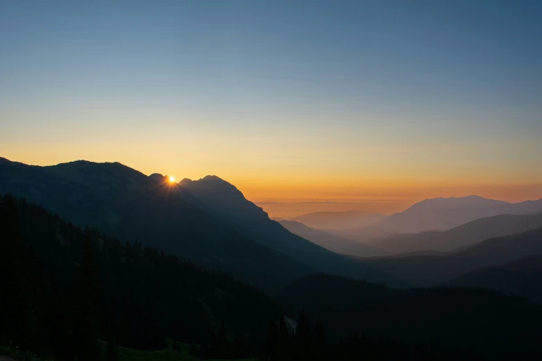 the sun rises on the mountains near a road