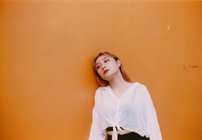a woman wearing white is leaning against a yellow wall