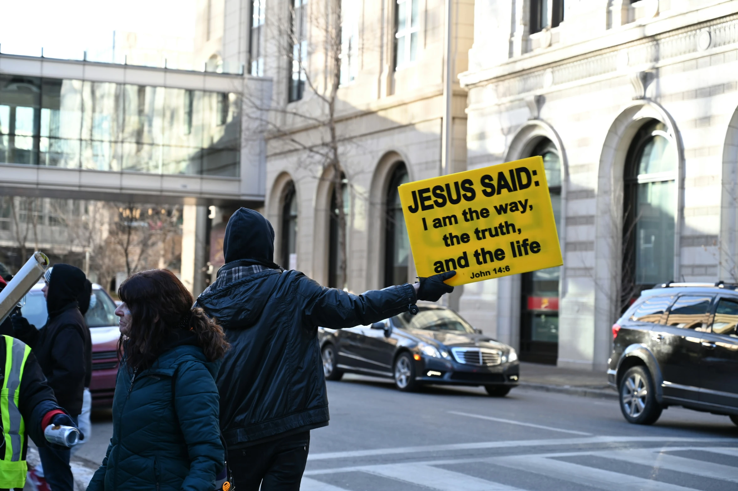 protesters in front of buildings holding a sign that says jesus said