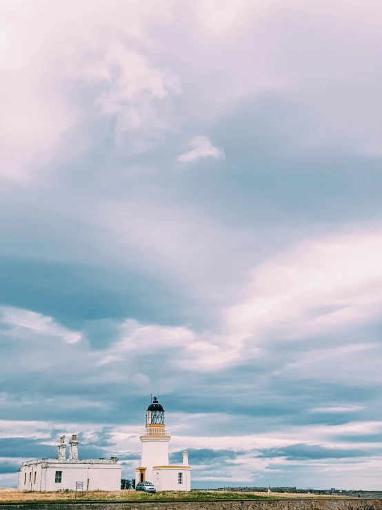 a white lighthouse on top of a hill with a cloudy sky above it