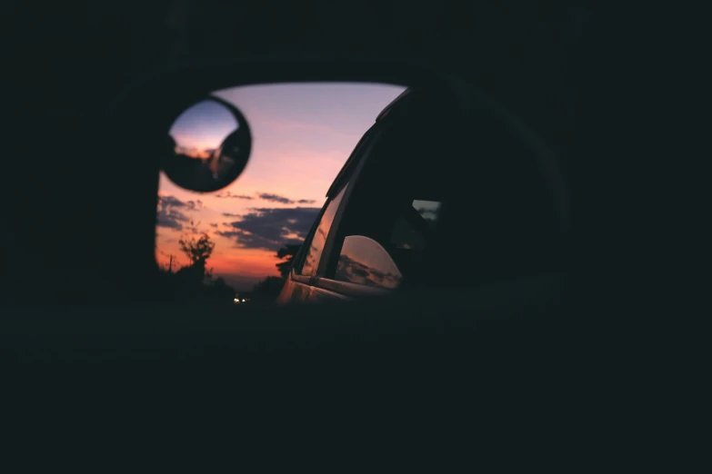 a rear view mirror reflecting a sunset in the side mirror