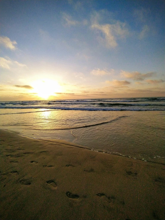 footprints in the sand at a beach with the sun setting